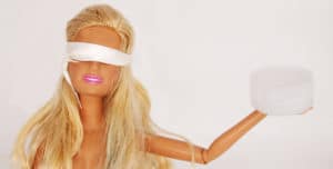 plastic doll wears a blindfold while holding a plastic bottle cap