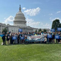 Coalition of many members standing outside the Capital, with signs and a banner