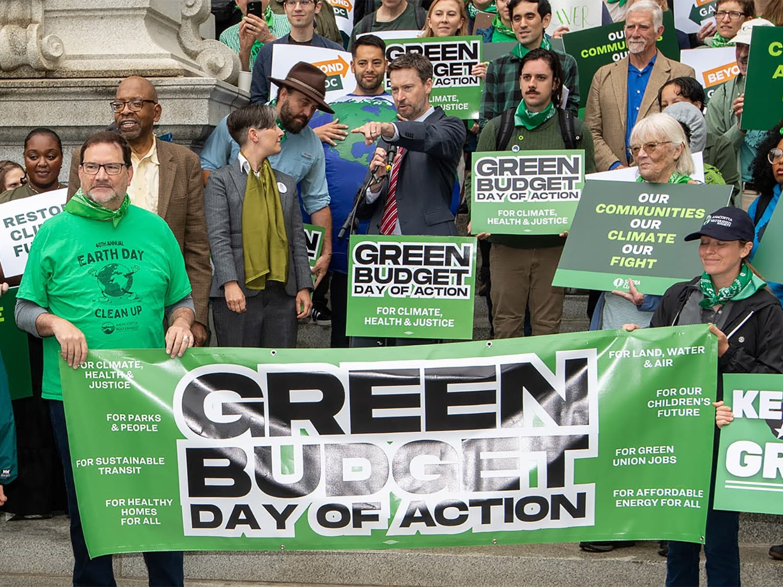 People stand on steps of DC City Hall holding banner of Green Budget Day of Action. Councilmember Charles Allen [center], joined by local and national environmental leaders, addresses the media during the DC Green Budget Day of Action.