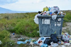 Garbage overflowing with plastic bags and waste in a green field