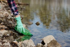 person picking up water bottle in creek