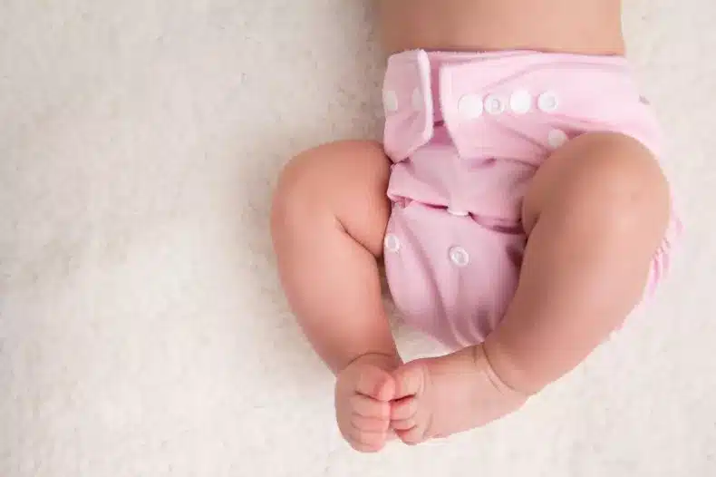 A baby lays on a bed wearing a cloth diaper. Aurora Uribe